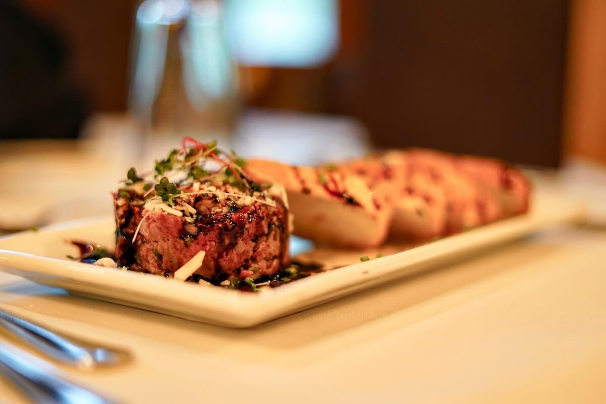 A plated dish featuring a serving of tartare topped with microgreens, reminiscent of the culinary charm found in the best towns to visit in Alabama, is accompanied by slices of toasted bread on a white rectangular plate.